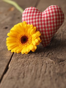 Checkered fabric heart shape with a yellow gerbera daisy on a rustic wooden table, Valentines Day or Mothers Day concept background with space for text