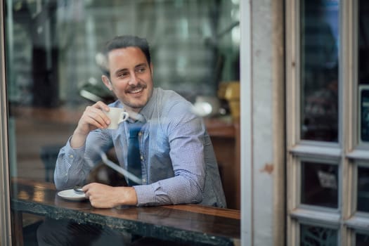Millennial businessman is laughing while enjoying a cup of coffee in a cafe before work.