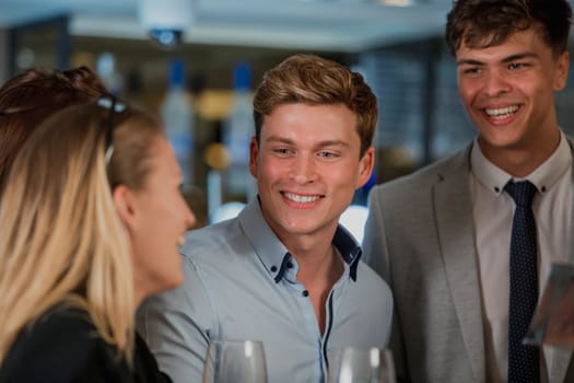 Coworkers are enjoying drinks in a bar after work. A man is holding a pint of beer and is talking to a woman who has her back to the camera.