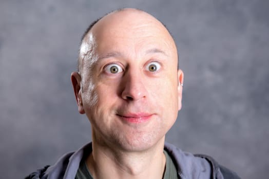 young baldheaded man in front of gray background looking amazed in to the camera
