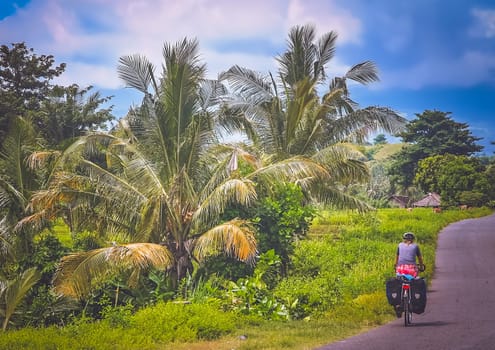 Female cyclist cycling through tropics in Lombok, Indonesia