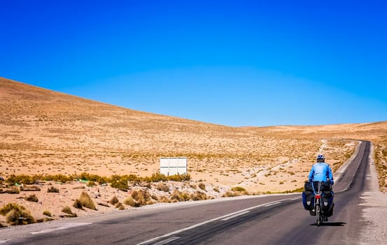 Woman cycling on the empty road to Parc National Lauca located on the border between Chile and Argentina, South America