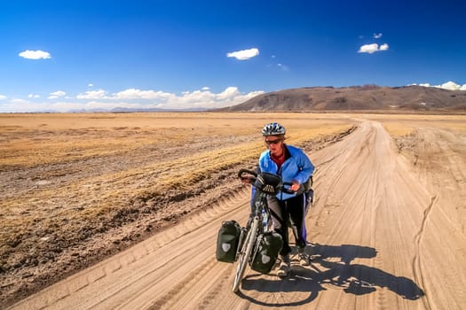 Woman cyclist struggling and pushing her bike on the sandy corrugated road in Altiplano in Bolivia
