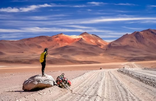 Cyclist takes a break standing on a big rock in the remote park of Altiplano in Bolivia