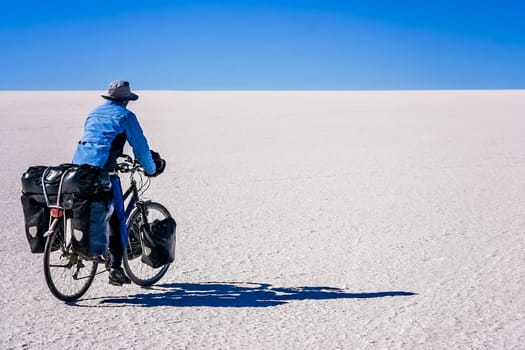 Lonely female cyclist travelling solo through the Salar de Uyuni in Bolivia, the biggest salar in the world
