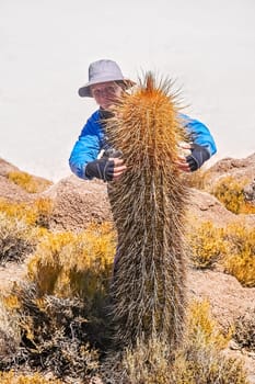 Woman posing with a single cactus growing on a rocky island in the middle of Salar de Uyuni, Bolivia