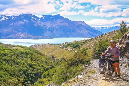 Cyclist pushing his bicycle uphill on a narrow rocky path at the end of the Carretera Austral, leading to the border between Chile and Argentina, South America