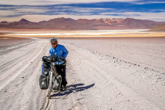 Woman cyclist struggling and pushing her bike on the sandy corrugated road in Altiplano in Bolivia