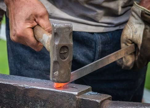 A blacksmith hammering hot iron during medieval fair festival in Streatham Park in London