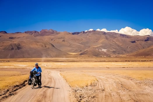 Woman cyclist struggling and pushing her bike on the sandy corrugated road in Altiplano in Bolivia