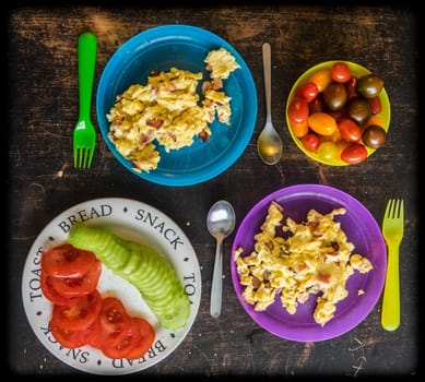 Two children plastic plates with scrambled eggs breakfast with bowl of cherry tomatoes on the side