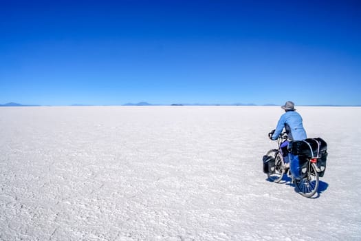 Lonely female cyclist travelling solo through the Salar de Uyuni in Bolivia, the biggest salar in the world