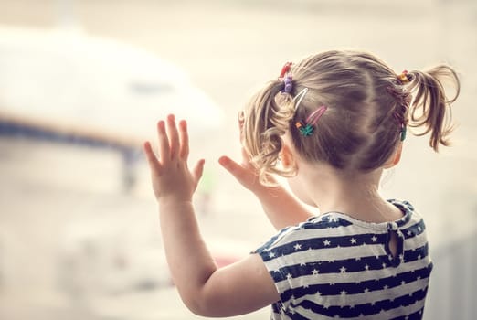 Little baby girl looking through the large window at the airport