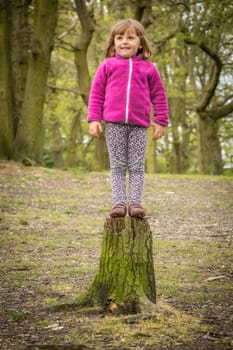 Little girl getting ready to jump from the cut tree in the forest