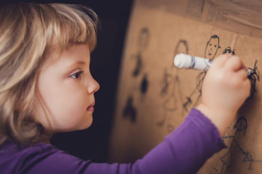 Little girl drawing on a cardboard at home
