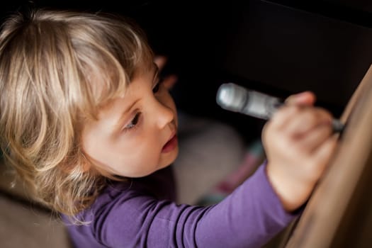 Little girl drawing on a cardboard at home