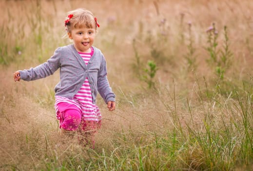 Baby girl walking among the high grass on a meadow in autumn
