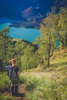 Caucasian girl with small backpack photographing the crater and cone of the Gunung Rinjani volcano, Lombok