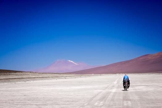 Lonely female cyclist travelling solo through the Salar de Uyuni in Bolivia, the biggest salar in the world