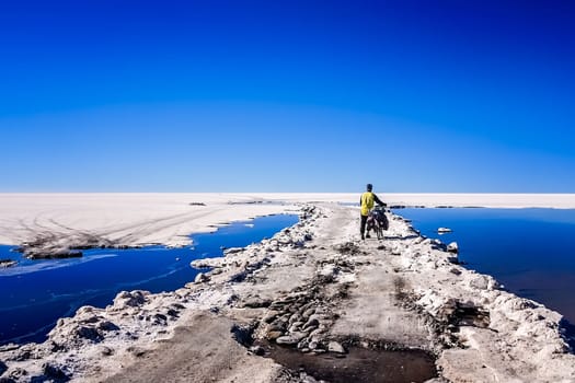 Lonely male cyclist travelling through the biggest salar in the world - Salar de Uyuni in Bolivia