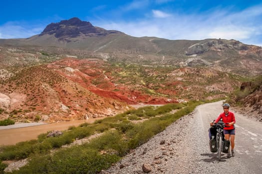 Woman pushing her bicycle uphill on a gravel stretch of the famous national Ruta 40 Quarenta in the remote part of central Argentina