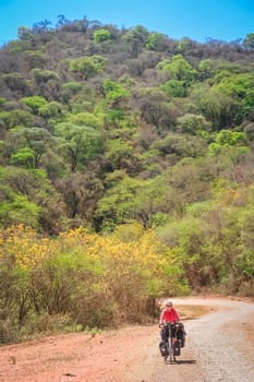 Woman cycling on the corrugated road through the tree covered hills Argentina