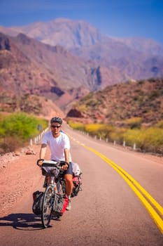 Man cycling on the empty road to Cafayate in the remote part of north west Argentina