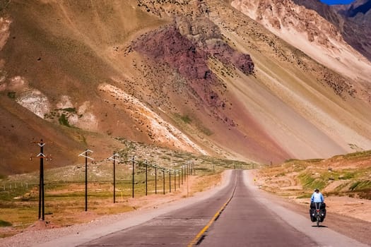 Woman cycling on the empty road from Mendoza in Argentina to Valparaiso in Chile, climbing constantly to the border and passing Park National Aconcagua on the way