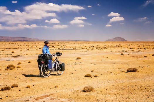 Woman cycling through the dry, desolate, empty countryside towards Oruro in central Bolivia