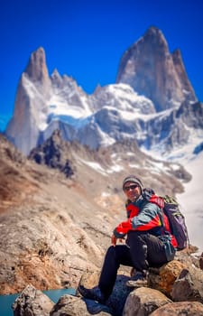 Male trekker resting on the rock in front of the stunning and impressive Mount Fitz Roy near El Chalten in Patagonia, Argentina
