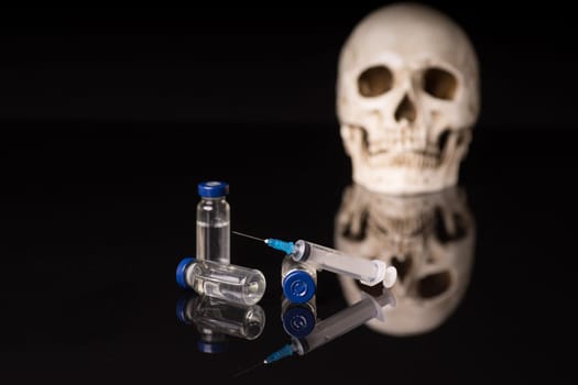 Skull, syringe and medical vials isolated on black blue background with glossy reflection