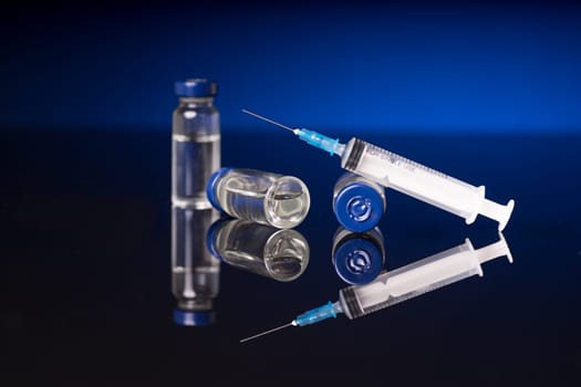 syringe and medical vials isolated on black blue background with glossy reflection