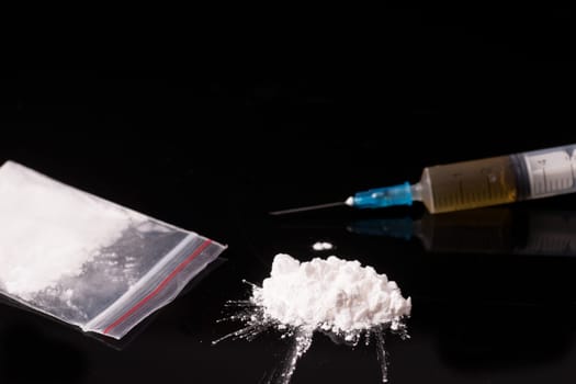 cocaine, Herion or other illegal drugs that are sniffed by means of a tube or injected with a syringe isolated on black glossy background