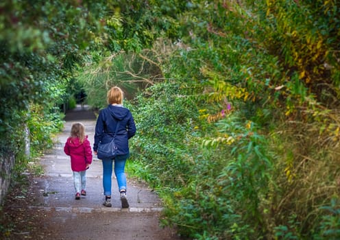 Mother and daughter walking together on a path in the countryside in autumn