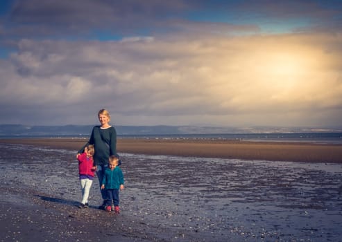 Mom with her daughter and son jumping up in the air together on a beach