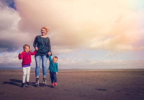 Mom with her daughter and son jumping up in the air together on a beach