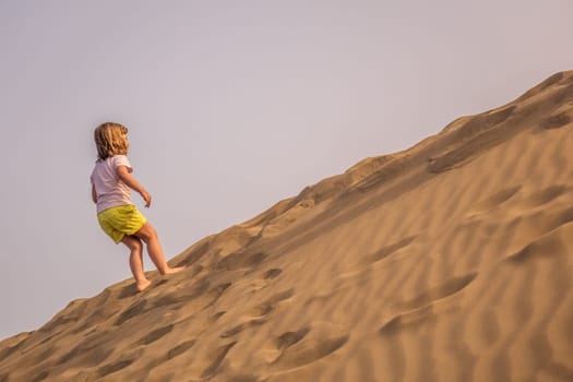 Little girl walking up the sand on the sand dunes in  the Natural Reserve of Dunes of Maspaloma in Gran Canaria