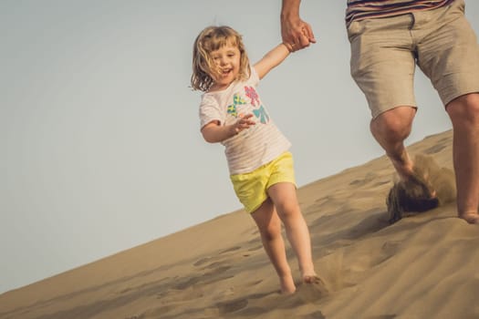 Little girl running down the sand dunes with her father in the Natural Reserve of Dunes of Maspaloma in Gran Canaria