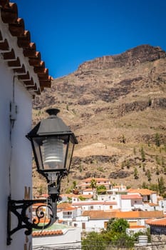 Lamp on a building wall with the tiled roofs on homes in a small town of Fataga in the background, Gran Canaria, Canary Islands, Spain