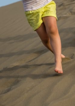 Little girl running down the sand dunes in  the Natural Reserve of Dunes of Maspalomas in Gran Canaria