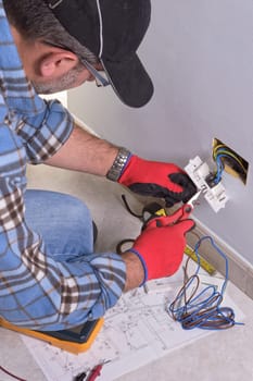 The technician wears the normal protective devices. Electrician's hands assembles a standard bipolar wall socket.