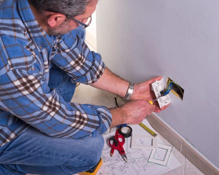 The technician wears the normal protective devices. Electrician's hands assembles a standard bipolar wall socket.