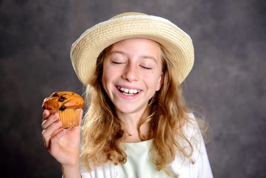 smiling girl with blond hair in white dress and straw hat eating muffin