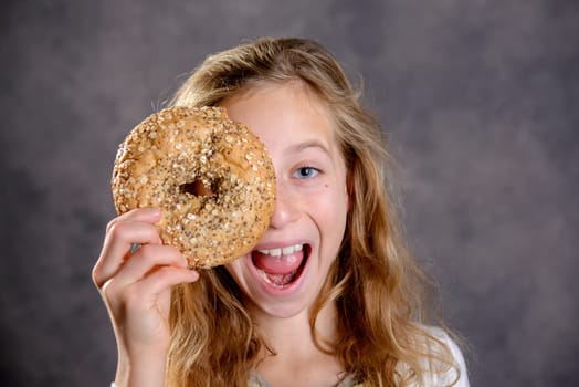 nice blond girl in front of gray background looking through a big bagel
