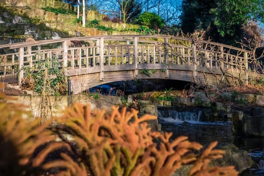 Wooden bridge in front of a small artificial waterfall in Regents Park, London