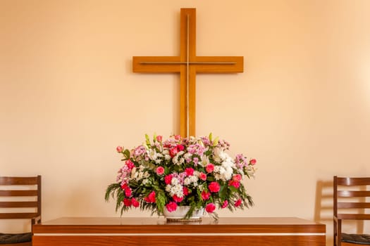 Christian cross, altar, candle and flower bouquet in a church chapel.