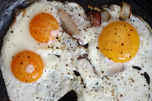 Detail of the fried eggs with bacon on the pan - a hearty breakfast