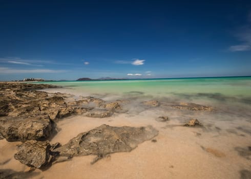 Beautiful turquoise blue sea in Corralejo Dunes National Park in Fuerteventura, Canary Island, Spain with Los Lobos Island in the background