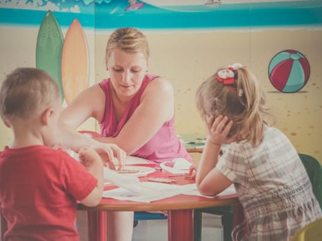 Woman and children drawing and coloring pictures during art time at the nursery
