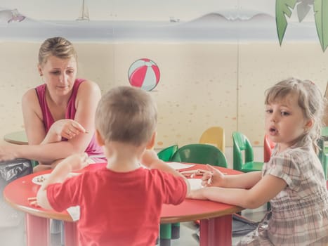 Woman and children drawing and coloring pictures during art time at the nursery
